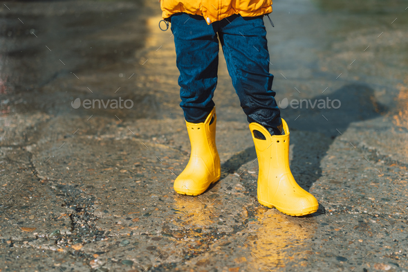 Boy in yellow rubber boots and wet jeans