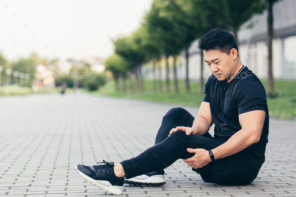 Asian man after fitness workout and jogging sits on the ground and suffers from leg pain - Stock Photo - Images