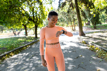 Female athlete runs in the morning in the park, looks at the fitness bracelet and rejoices