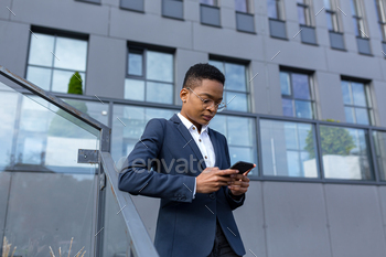 Business woman using cellphone, serious african american worker outside office