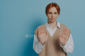 Displeased young 30s red haired woman showing NO gesture, isolated on blue background