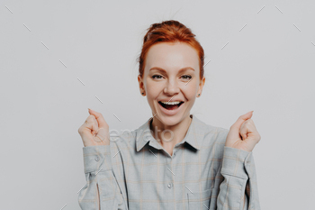 Happy excited red haired woman holding clenched fists and celebrating success in studio
