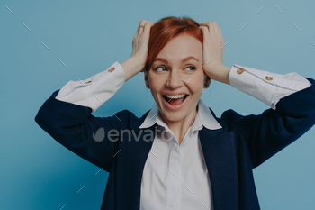 Young amazed excited businesswoman in formal wear hearing amazing news, holding head in both hands