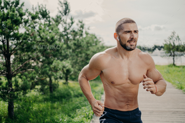 Sporty athletic man runs outdoor with naked torso, leads healthy lifestyle, has morning workout