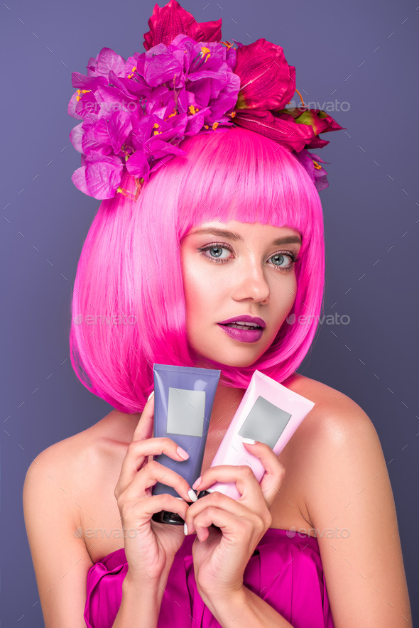 beautiful young woman with pink bob cut and flowers in hair holding tubes of coloring hair tonics