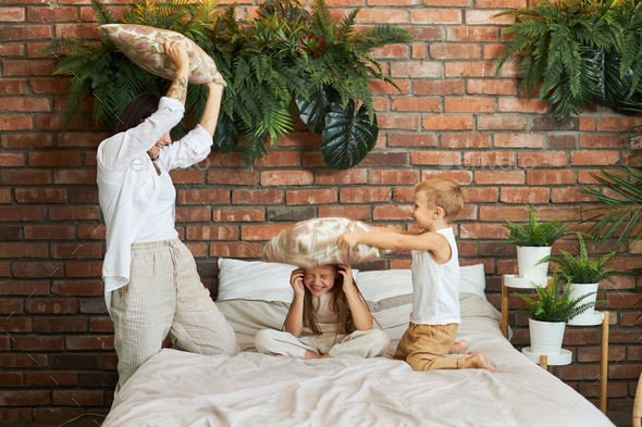Family leisure. Mom son and daughter fight on pillows on the bed in the bedroom. Joy and fun