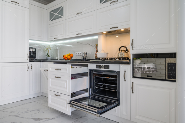 Luxurious white modern kitchen interior, drawers pulled out, oven's door open