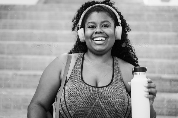 Sport curvy black woman listening music with headphones - Focus on face - Black and white editing