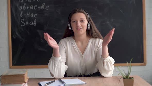 Young Caucasian Girl Student Sits at a Table in Headphones with a Microphone Looks at the Camera alt