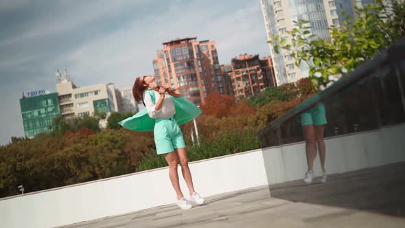 Beautiful woman in trendy turquoise suit spinning with happiness background city alt