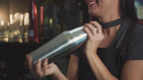 Smiling mixologist shaking craft cocktail in speakeasy bar, tilt down. alt