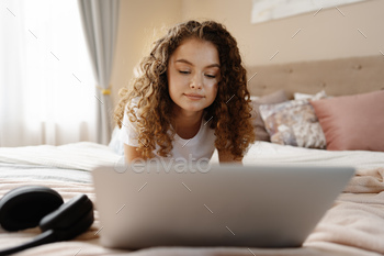 Portrait of a young curly woman using laptop in bed at home