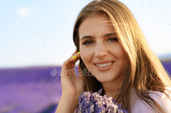 Young woman in dress holding bouquet of flowers standing in lavender field