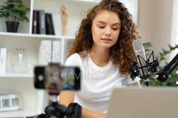 Young curly female blogger recording video at table at home