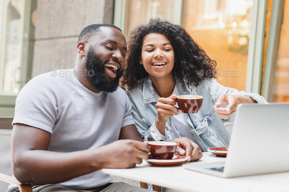 Cheerful african-american young romantic couple friends watching movie comedy online