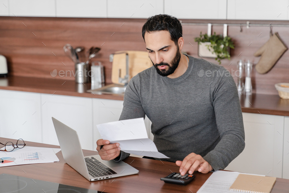 Busy concentrated Arabian man freelancer student counting calculating costs, expenses