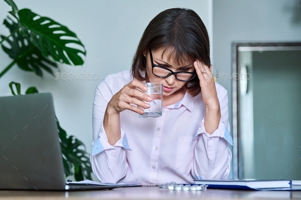 Tired middle-aged woman suffering from headache at workplace with laptop - Stock Photo - Images