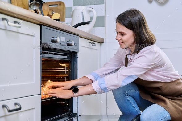 Young woman cooking food in the oven at home in the kitchen. - Stock Photo - Images