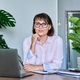 Middle aged woman looking at camera sitting at her desk with laptop - PhotoDune Item for Sale