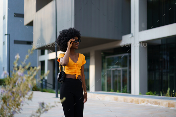 Photo of a stylish young black woman with curly hair wearing orange crop top walking in the street
