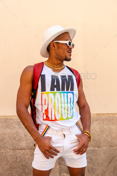 Portrait of a gay black ethnicity man at the pride party on a cream wall, LGBT flag, vertical photo