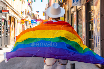 A gay black man walking in the pride party with an LGBT flag, on his back