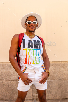 Portrait of a gay black ethnicity man at the pride party on a cream wall, LGBT flag, vertical photo