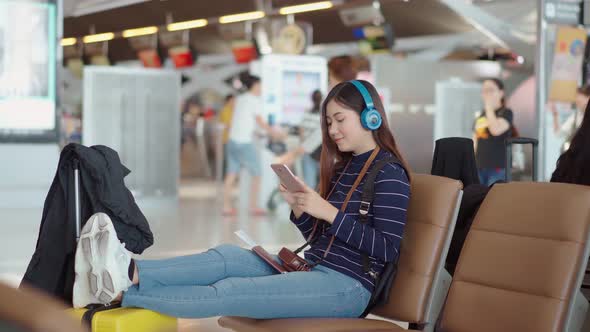 Young female traveler listening music from headphone at airport