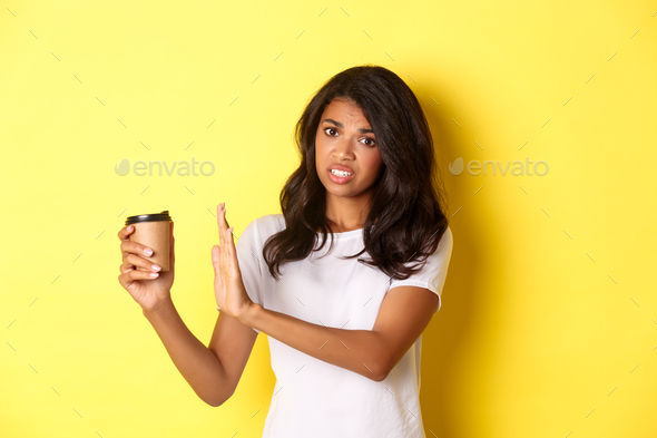 Image of african-american girl complaining about bad taste of coffee, showing reject sign and