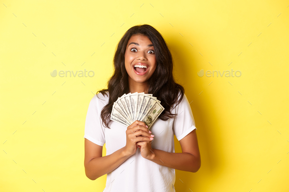 Image of beautiful, excited african-american girl, winning money prize and smiling, holding cash and