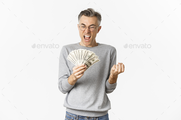 Image of cheerful middle-aged man in glasses and gray sweater, winning money, holding cash and