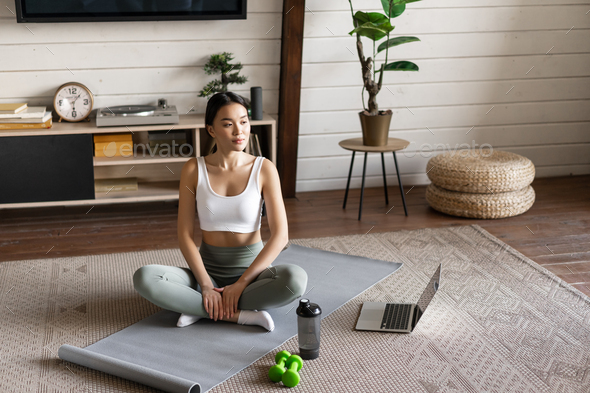 Asian fitness girl doing workout at home with laptop guide, sport application on computer, sitting