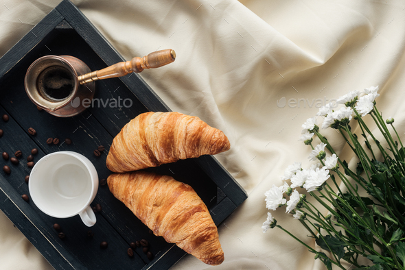 top view of coffee and croissants on tray on beige cloth with field flowers, breakfast in bed