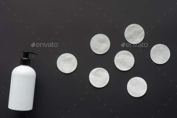 top view of bottle of lotion and cosmetic pads isolated on black, beauty concept