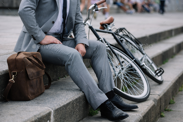 cropped view of businessman in grey suit sitting on stairs with bike