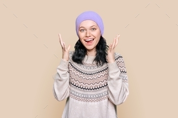 Happy emotional teenage female in sweater hat on light brown background