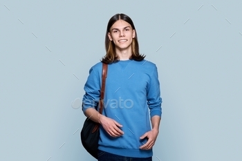 Portrait of young guy with backpack on gray background