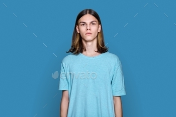 Portrait of serious teenage guy looking at camera on blue background