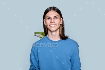 Portrait of young male with green parrot on his shoulder on gray background