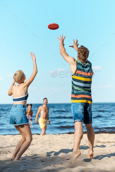 selective focus of multiracial friends playing with flying disc together on beach