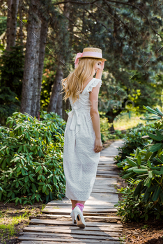 back view of beautiful girl in white dress and wicker hat walking on wooden walkway in park