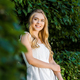 selective focus of beautiful smiling blonde girl in white dress posing near green leaves - PhotoDune Item for Sale