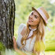 selective focus of beautiful girl in dress and wicker hat leaning at tree and looking away - PhotoDune Item for Sale