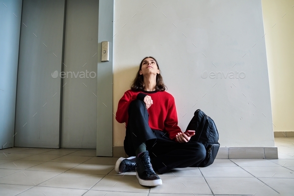 Sad teenage guy sitting on floor near elevator inside building