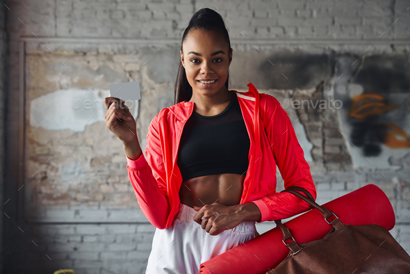 Happy young African woman in sports clothing holding gym card