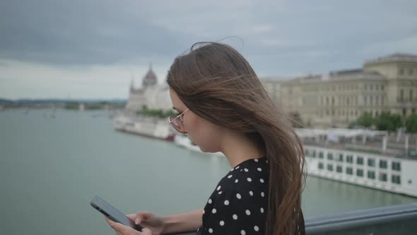 Townswoman is Typing Message on Mobile Phone on Szechenyi Bridge in Budapest alt
