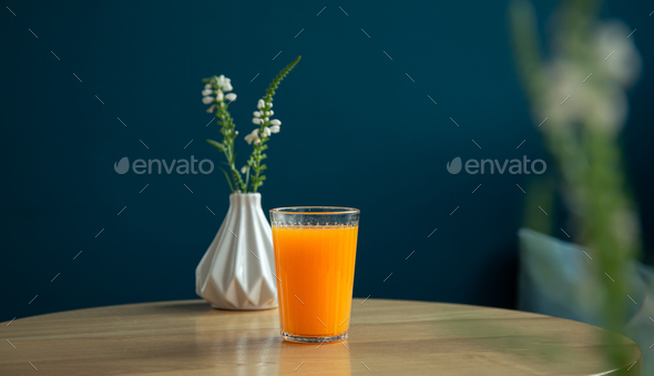 A glass of orange juice on a table in a blue interior. Stock Photo by  puhimec