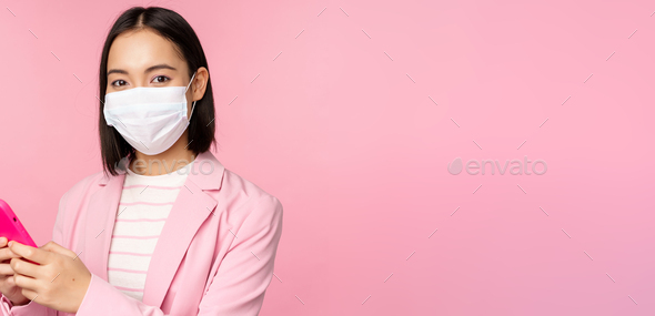 Asian businesswoman in medical face mask using mobile phone. Japenese saleswoman, corporate lady in