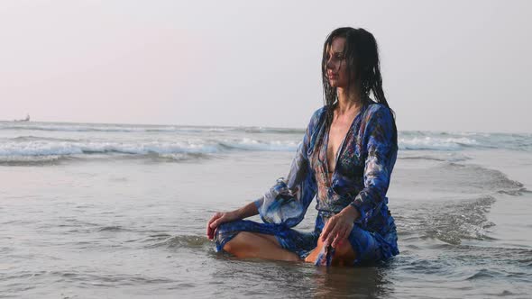 Young Wet Woman Sitting in Water at Sandy Beach and Doing Meditation Practices