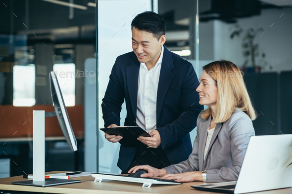 Two Asian male and female colleagues in a modern office, a woman shows ...